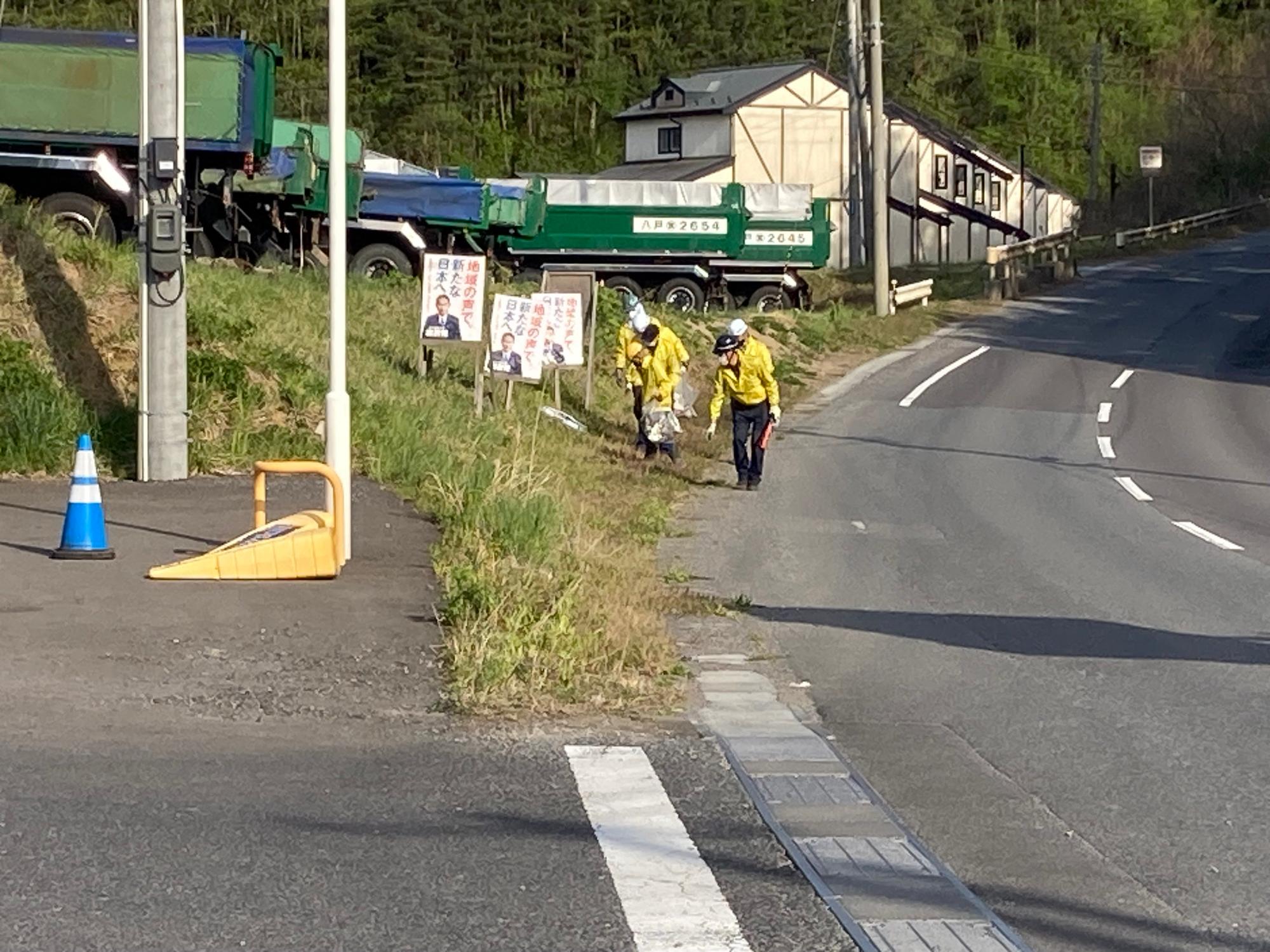 写真奥に建物とトラックの見える場所で道路脇のごみを拾っている写真