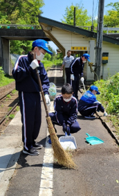 竹箒で駅のホームをはいている生徒の写真