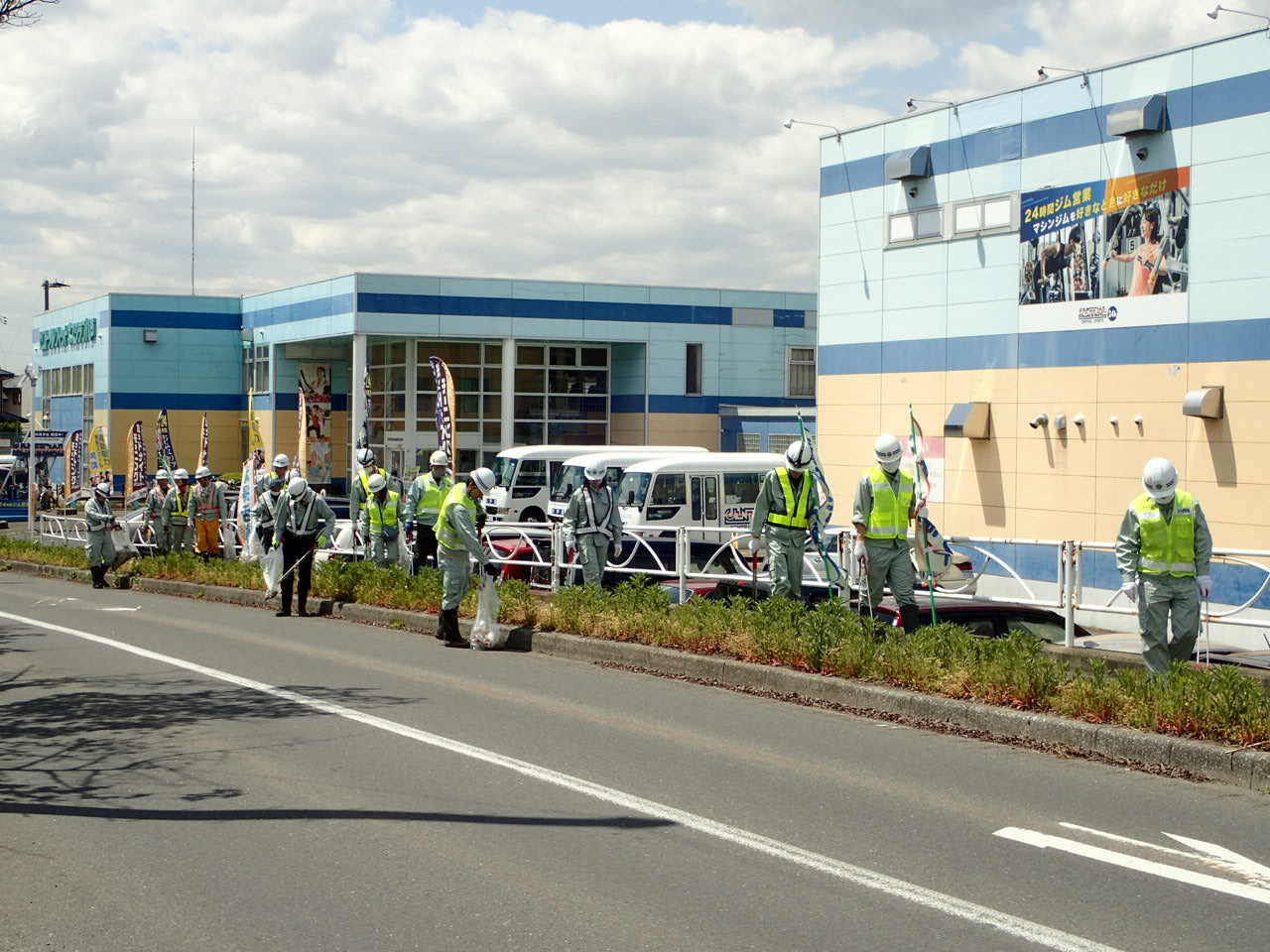 建物と道路の間の木や草のある場所でゴミを拾う人たちの写真