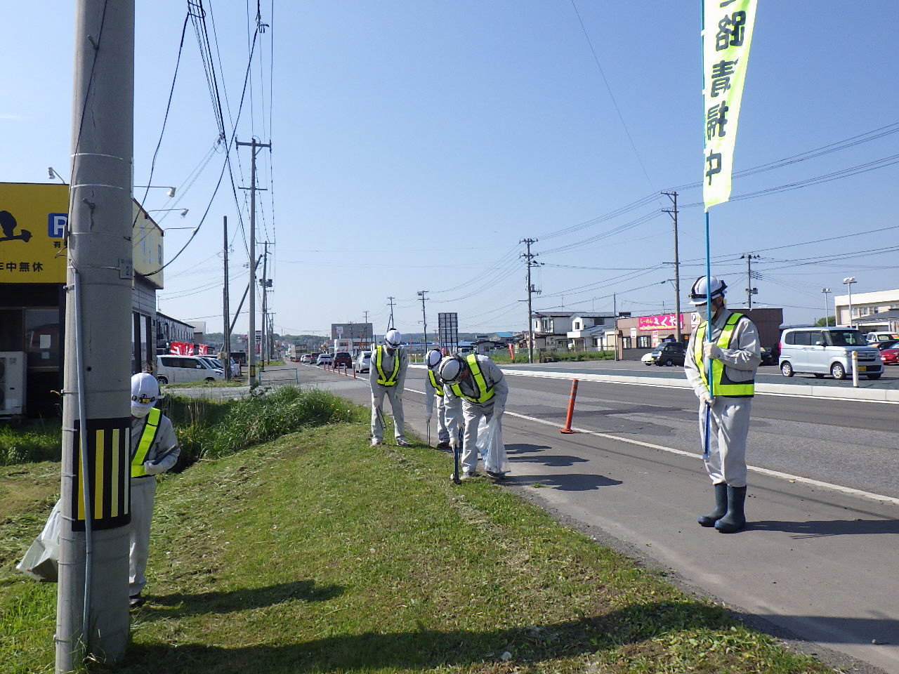 道路清掃中ののぼりを掲げて道路脇のごみを拾っている写真