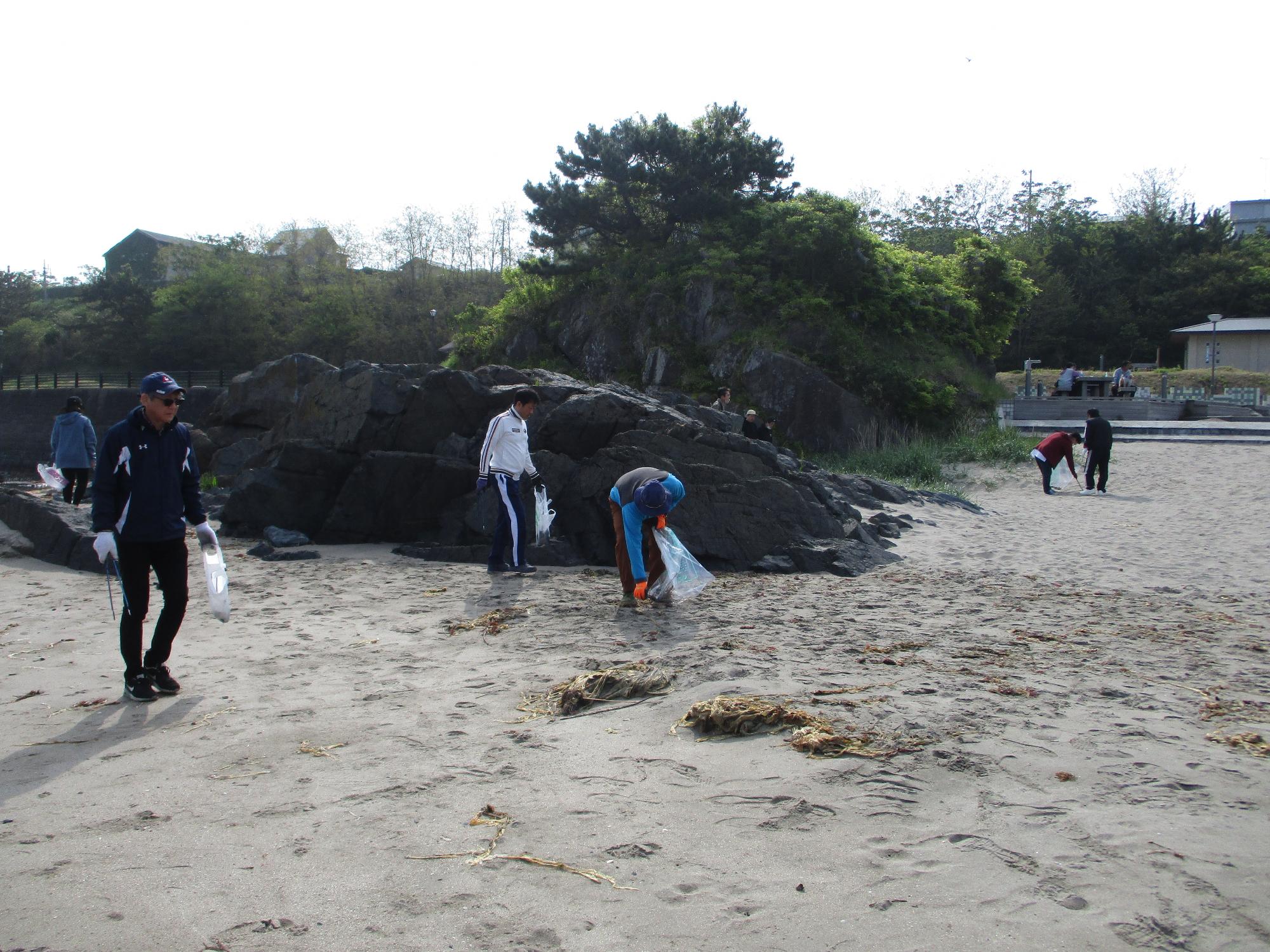 大きな岩の周りの砂地でごみを集める人たちの写真