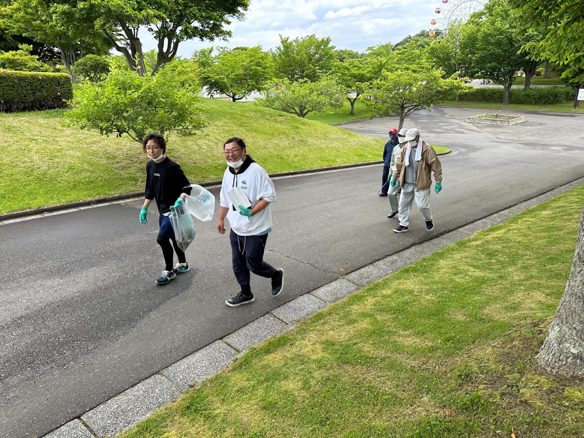 ボランティア用ごみ袋を手に公園内を歩く四人の写真