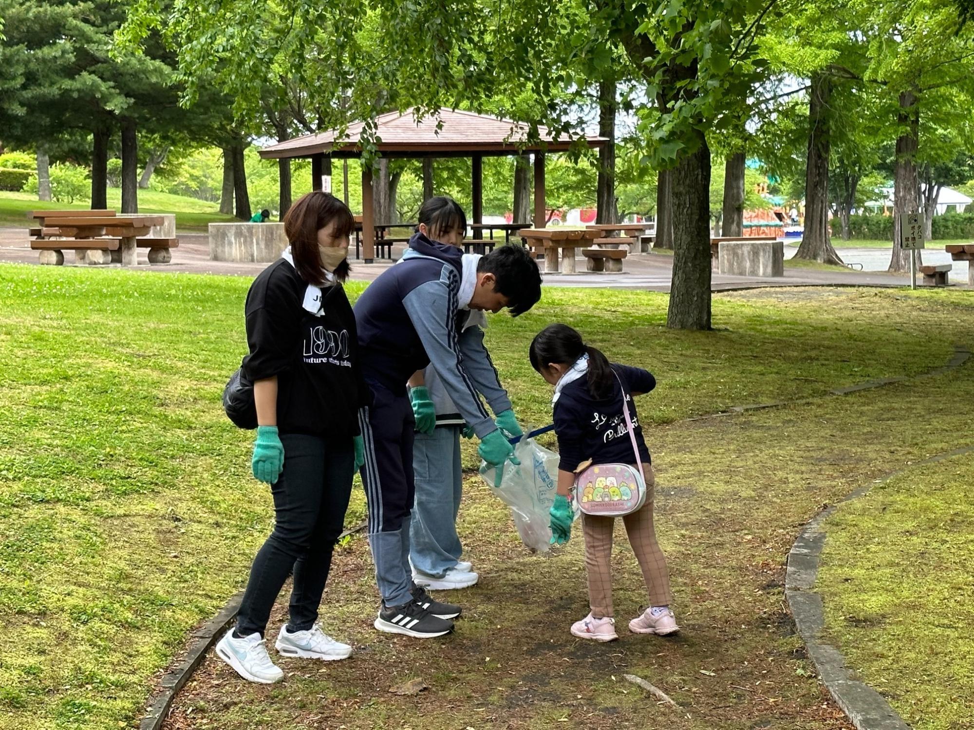 東屋の見える芝生地でごみを拾う親子とみられる四人の写真