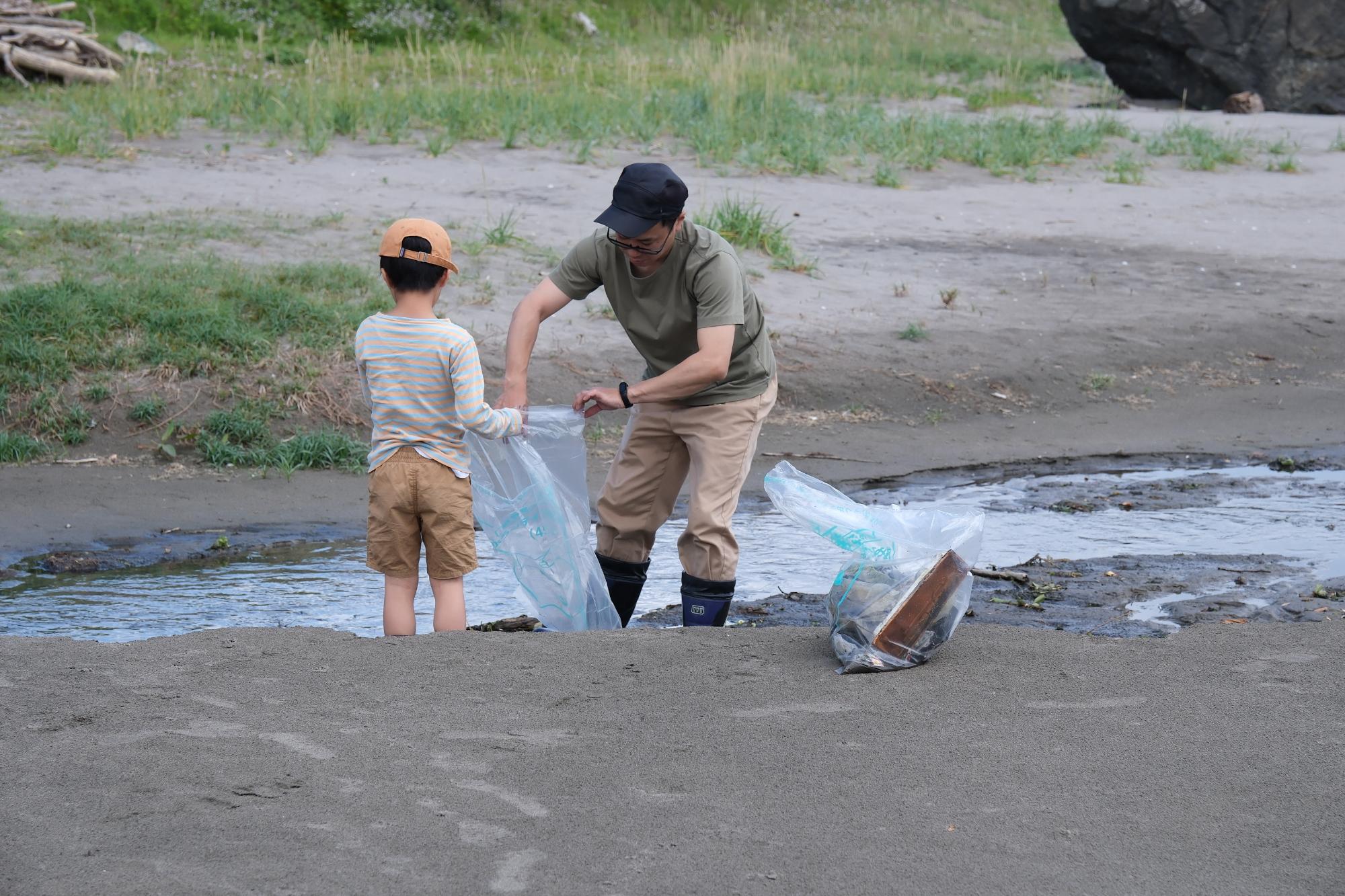 砂浜で子どもと男性が拾ったごみをボランティア用ごみ袋に入れている写真