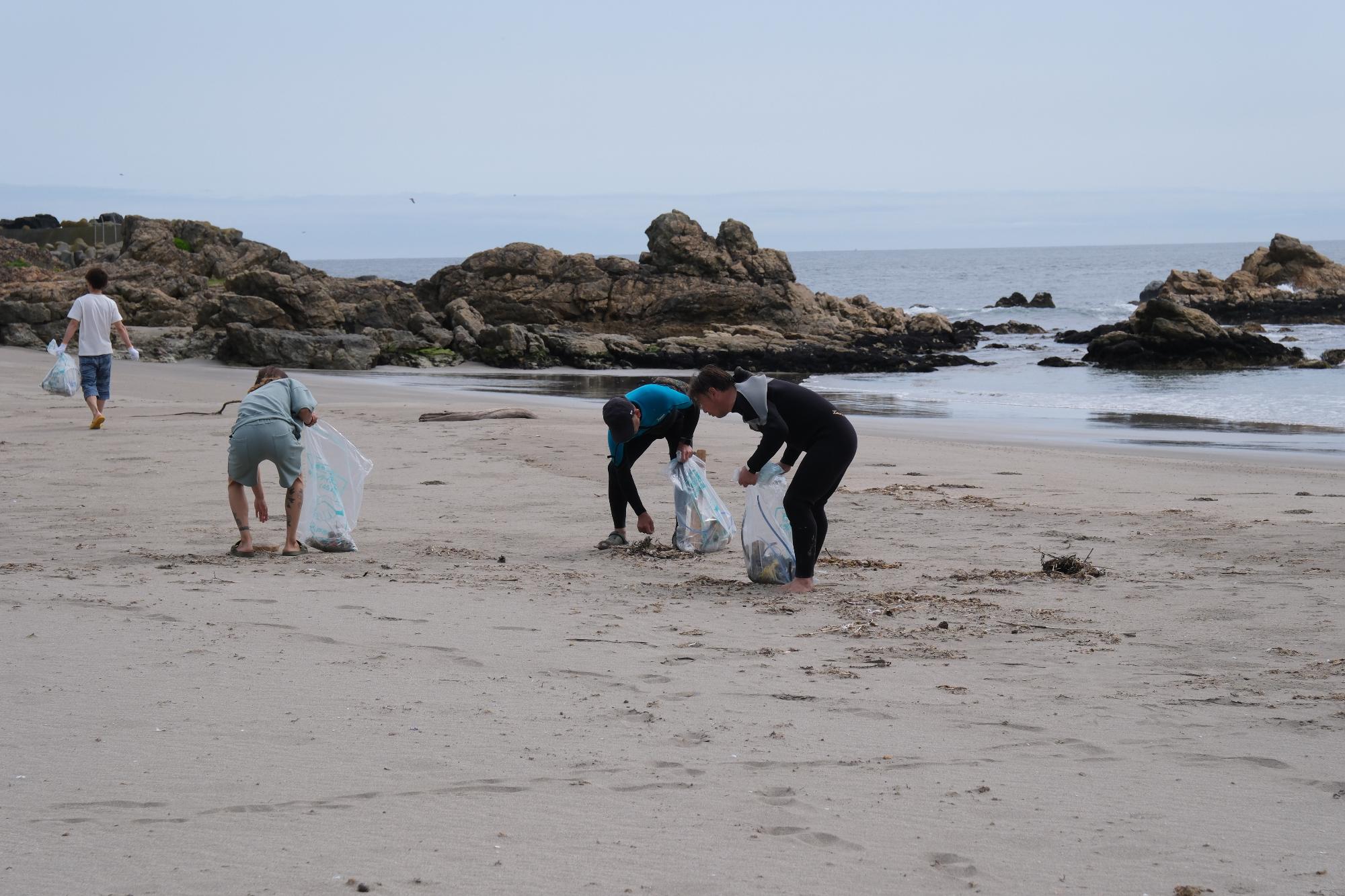 海をバックに砂浜でごみを拾う4人の写真
