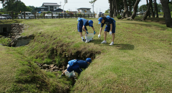 種差芝生地の段差のある場所でごみを拾っている三人の生徒の写真