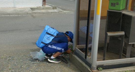 公衆電話ボックスの下のごみを拾おうとしゃがんでいる生徒一人の写真