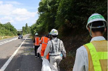 歩道を歩く作業服に反射ベストを着た人たちの写真