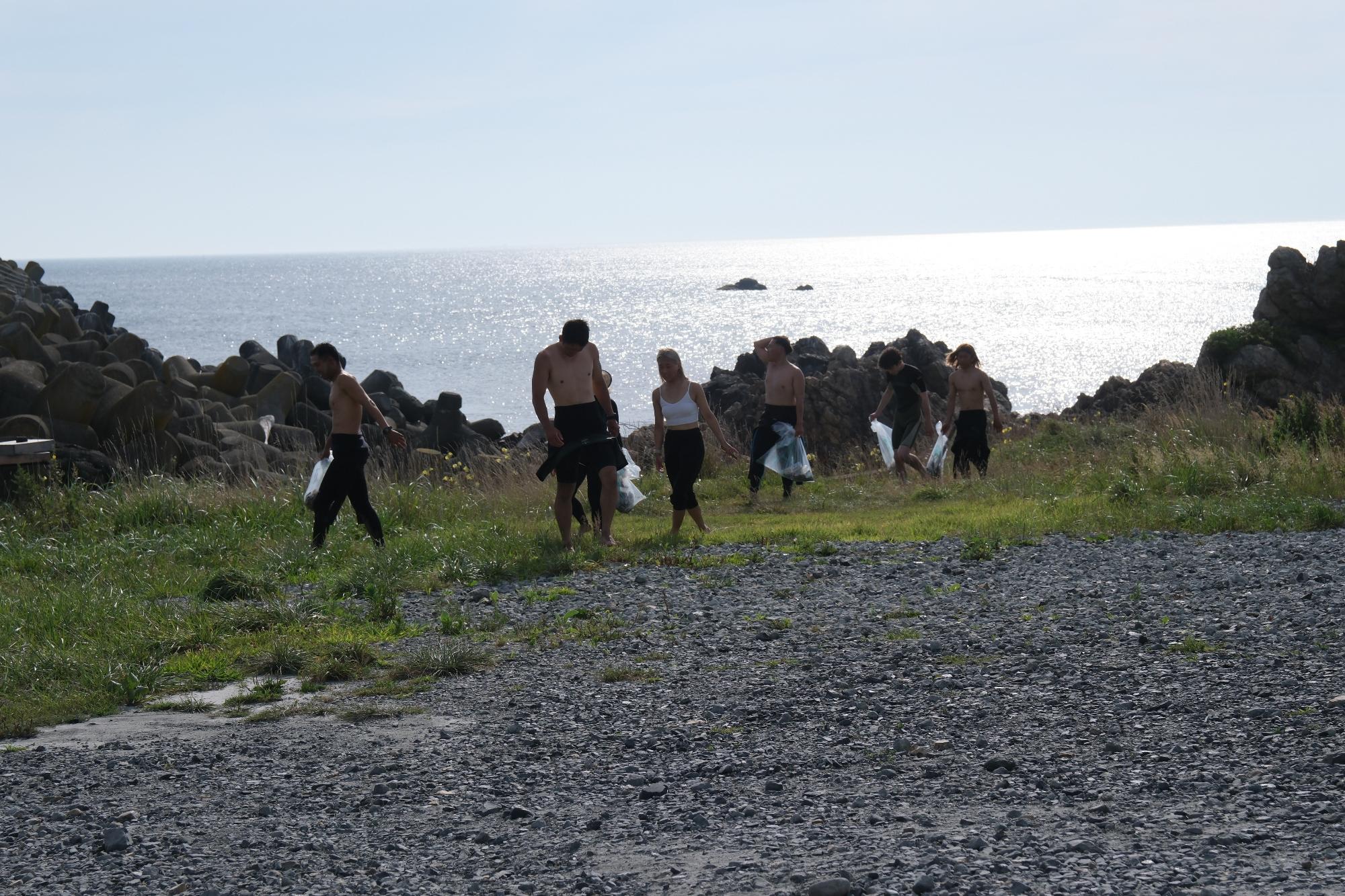海をバックに、上半身裸でボランティア用ごみ袋を手に活動するサーファーの人たちの写真