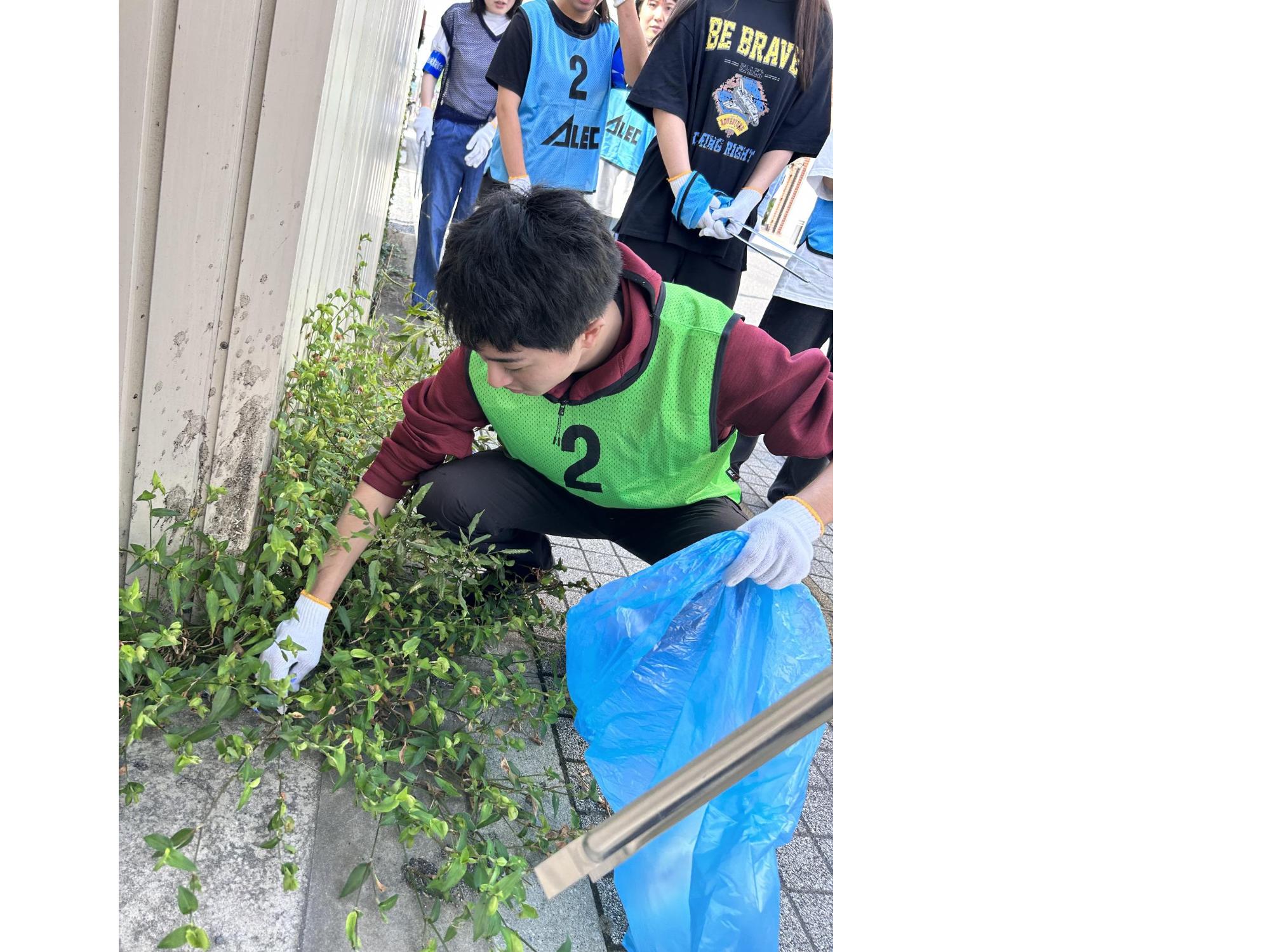 歩道の草の下のごみを手で拾っている男性の写真