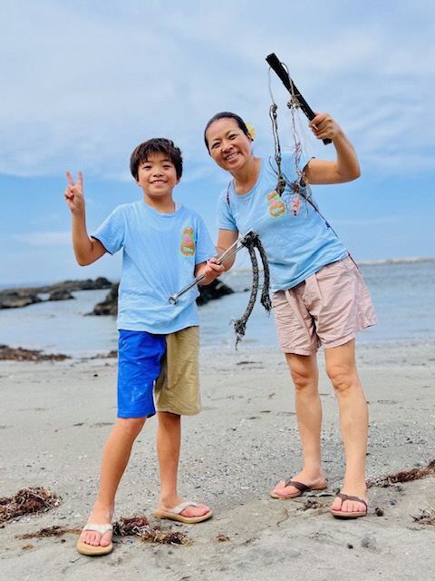 青い空と海をバックに、砂浜でトングで拾ったごみを手にしている女性と男児の写真