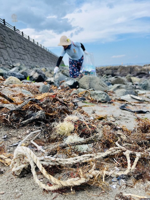 砂浜に打ち上げられた海藻の絡んだ漁網と、岩場のごみ