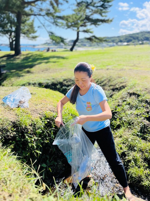 芝生地の水が流れている場所のごみを拾い、ボランティア用ごみ袋に入れている女性の写真