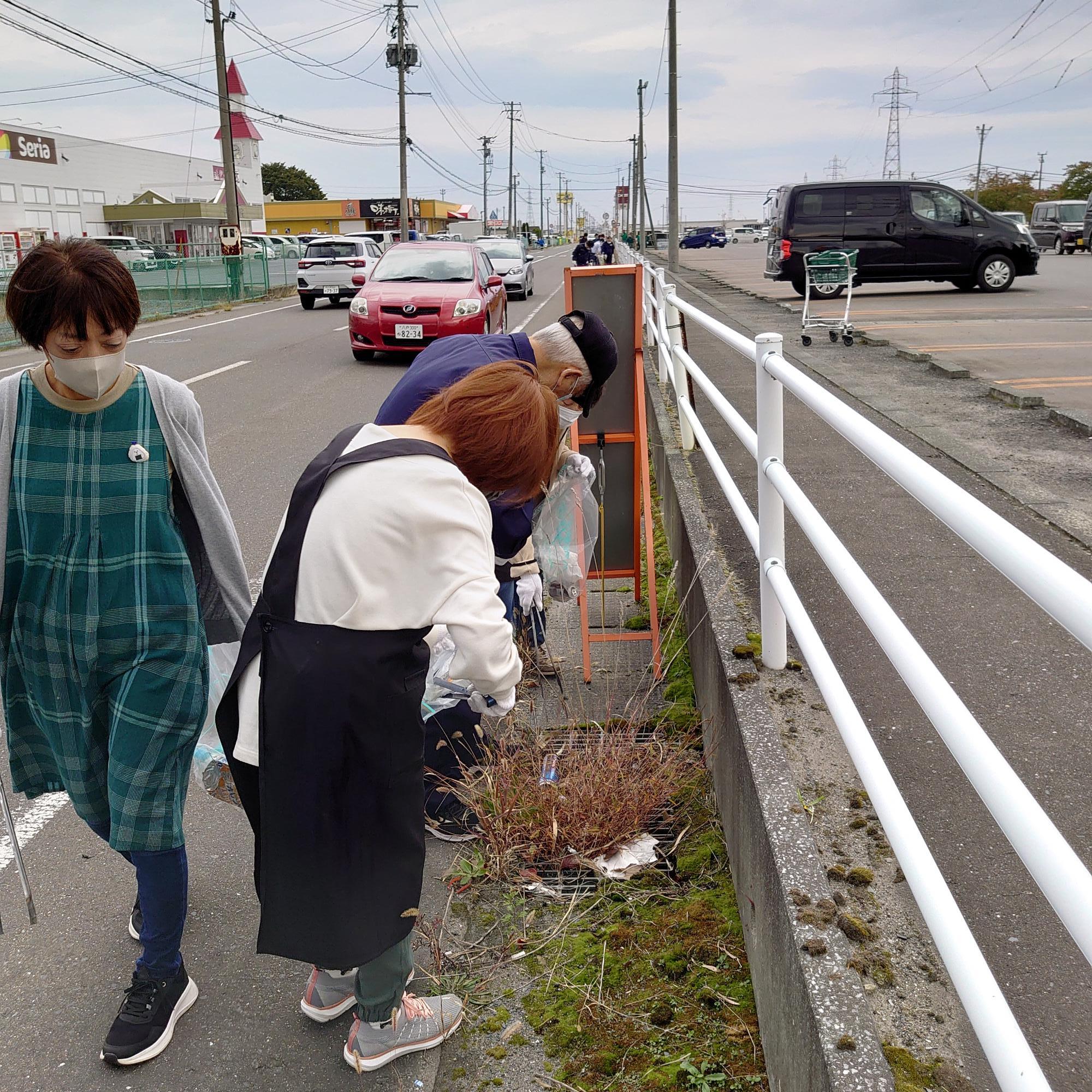 道路脇のごみを拾っている三人の写真