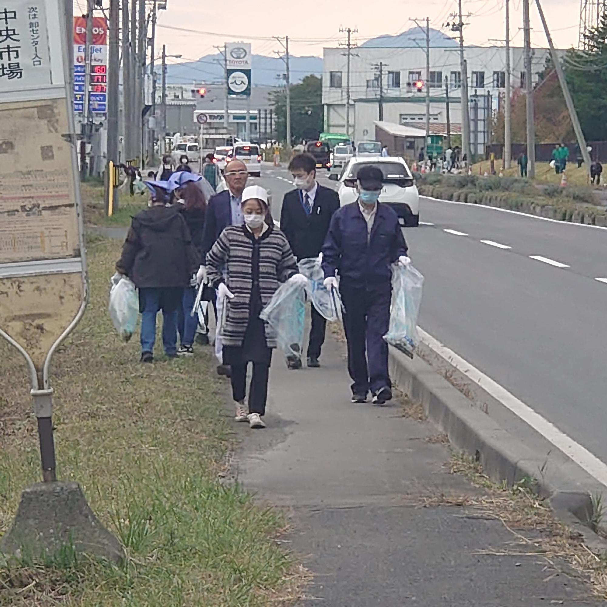 バス停近くの歩道をごみを拾って歩いている写真