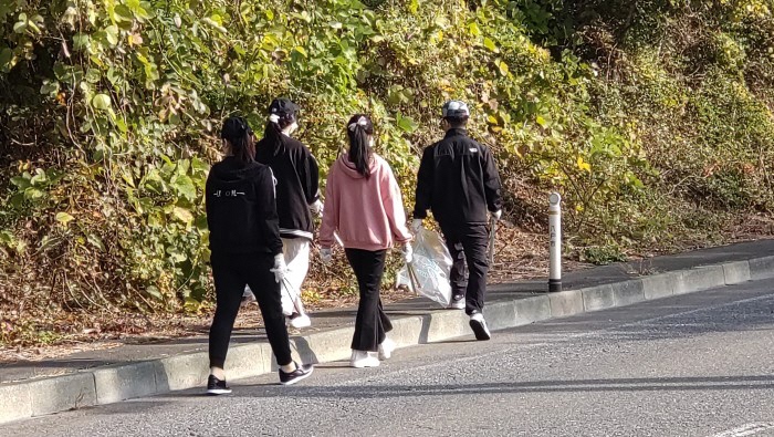 ボランティア用ごみ袋とトングを手に、道路脇を亜歩く4人の写真