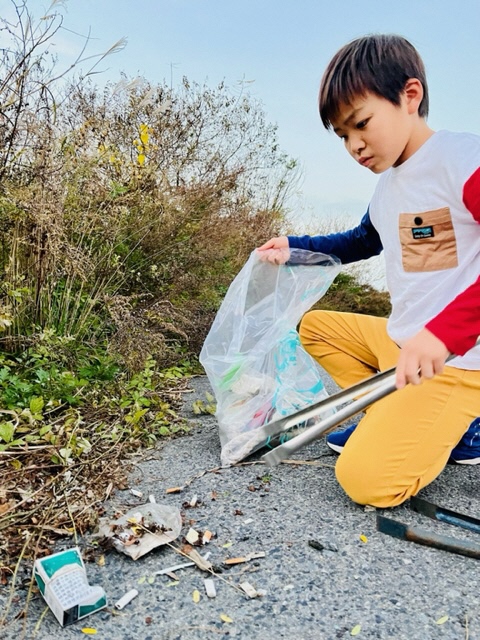 ポイ捨てされたタバコの空き箱をトングで拾っている男児の写真