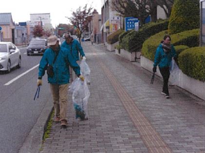 トングとボランティア用ごみ袋を手に持って歩道のごみを拾っている三人の写真