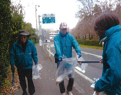 歩道で拾ったごみをトングで別の人の広げたボランティア用ごみ袋に入れている写真