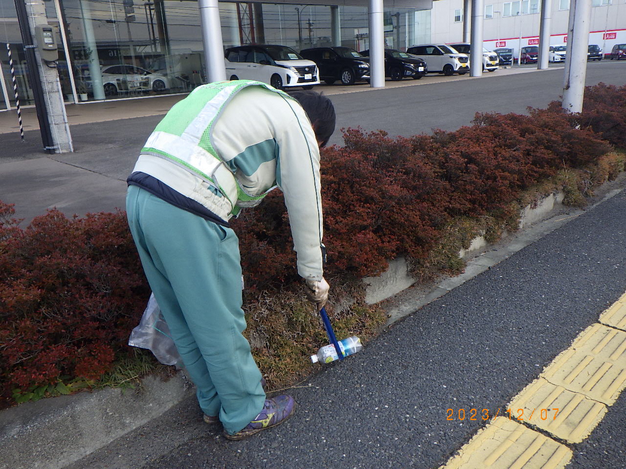 歩道の植え込み脇のポイ捨てされたペットボトルを拾っている様子