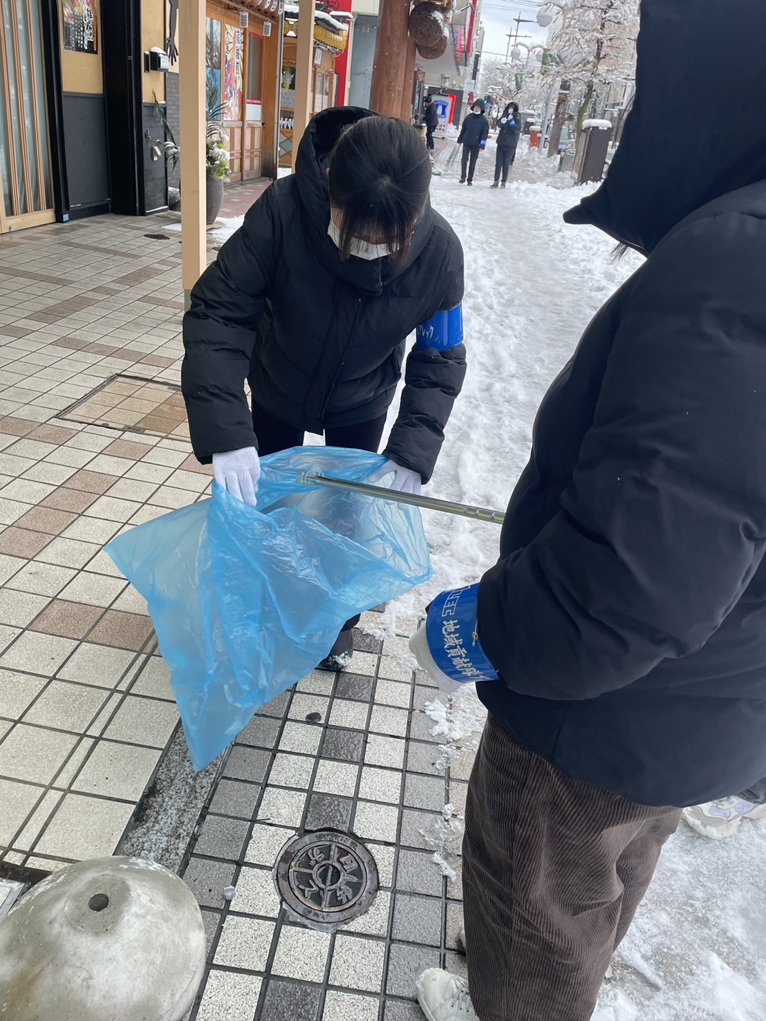 歩道で拾ったごみを袋に入れている二人の写真