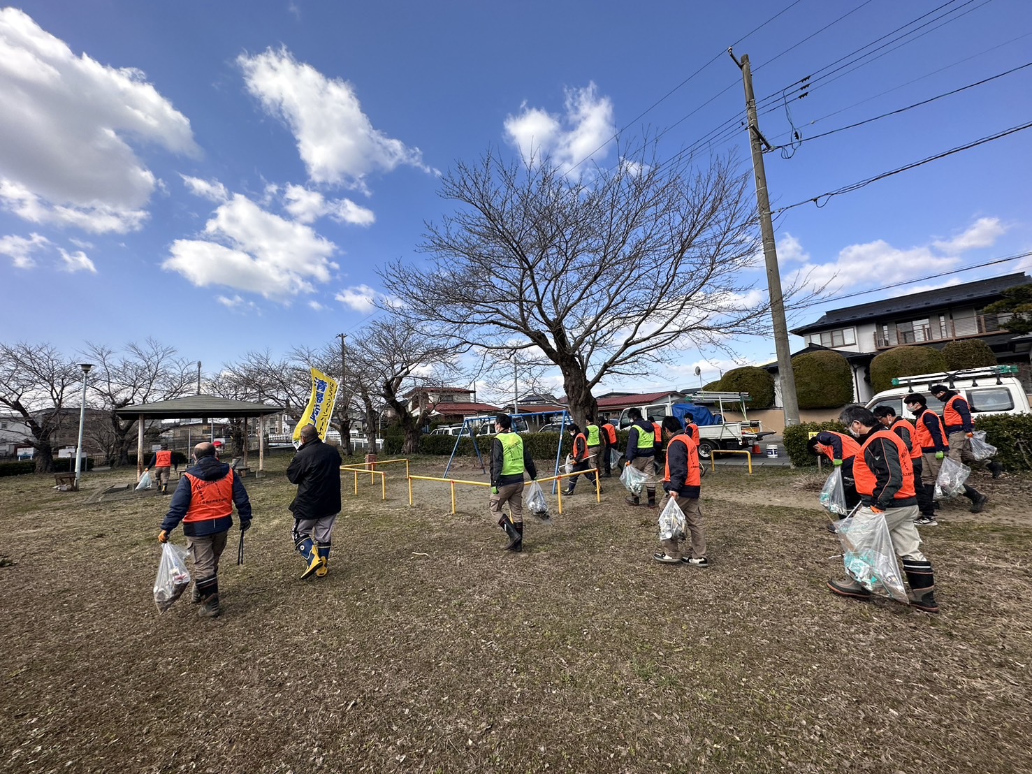青空の公園をビブスを着用しボランティア用ごみ袋を手に活動している写真。