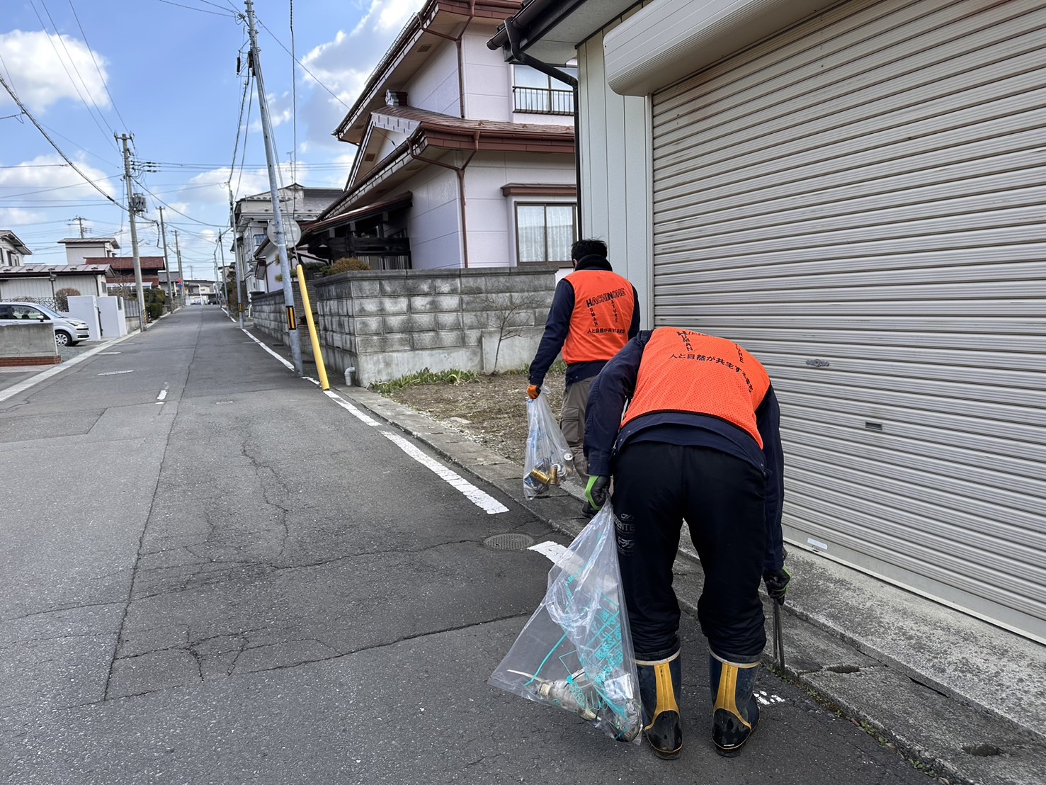 住宅地の道路脇のごみを拾う、ビブスを着用した男性の写真。