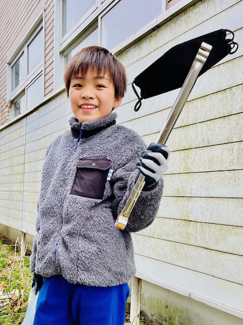 拾った黒いマスクをトングで掴んで見せている男児の写真