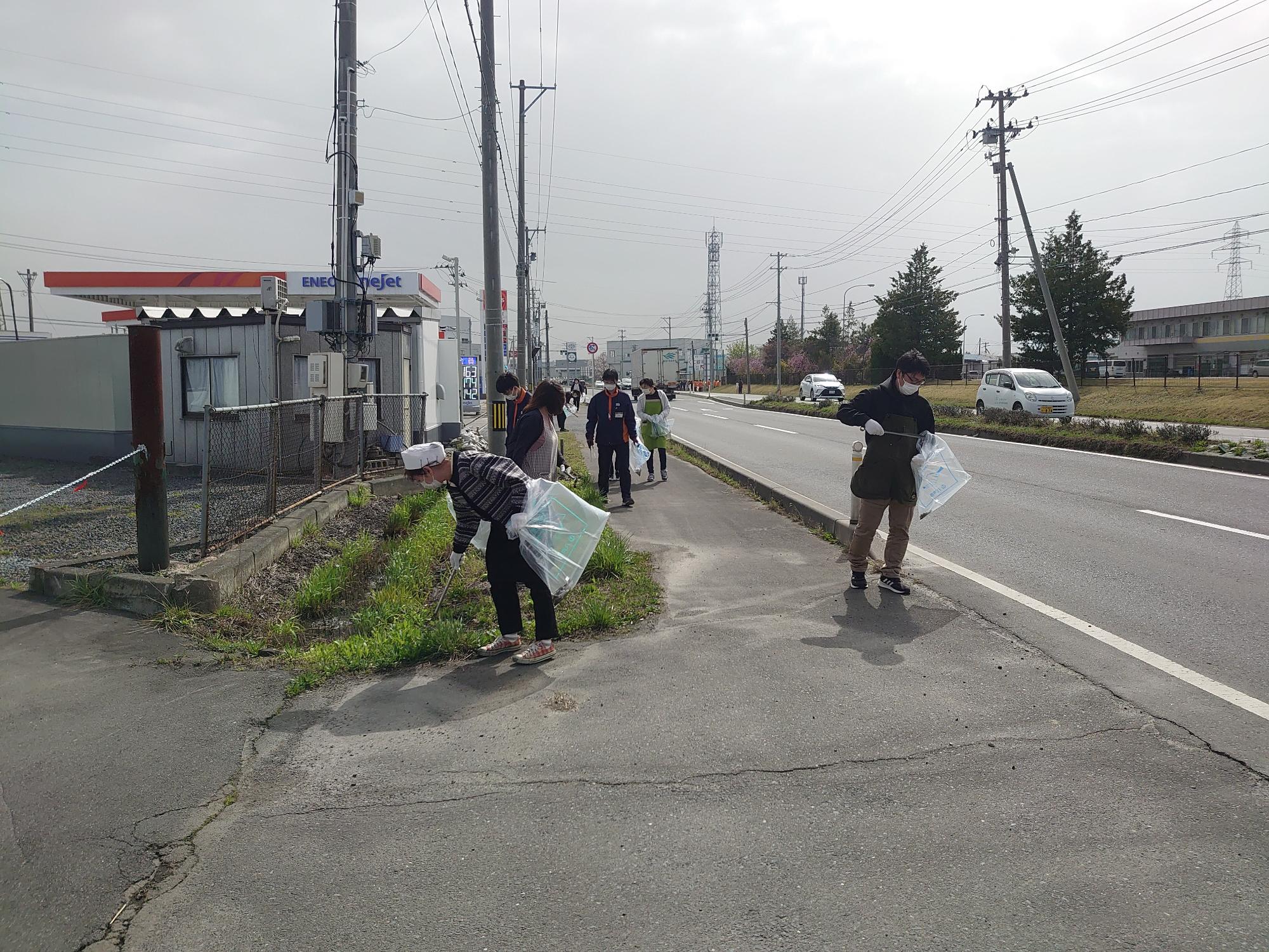 歩道の草地からトングでごみを拾う数人の写真