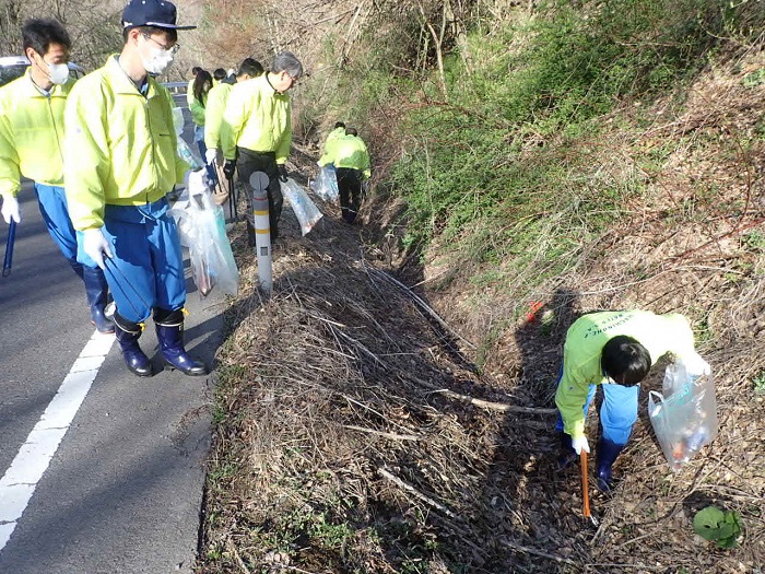 黄色いジャンパーを着て道路脇のごみを拾う多くの人の写真