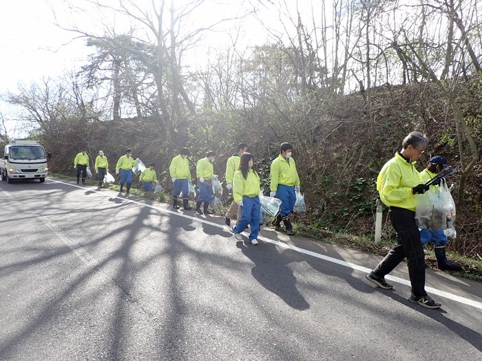 揃いの黄色いジャンパー、青いズボンで道路脇を歩く、11人の写真
