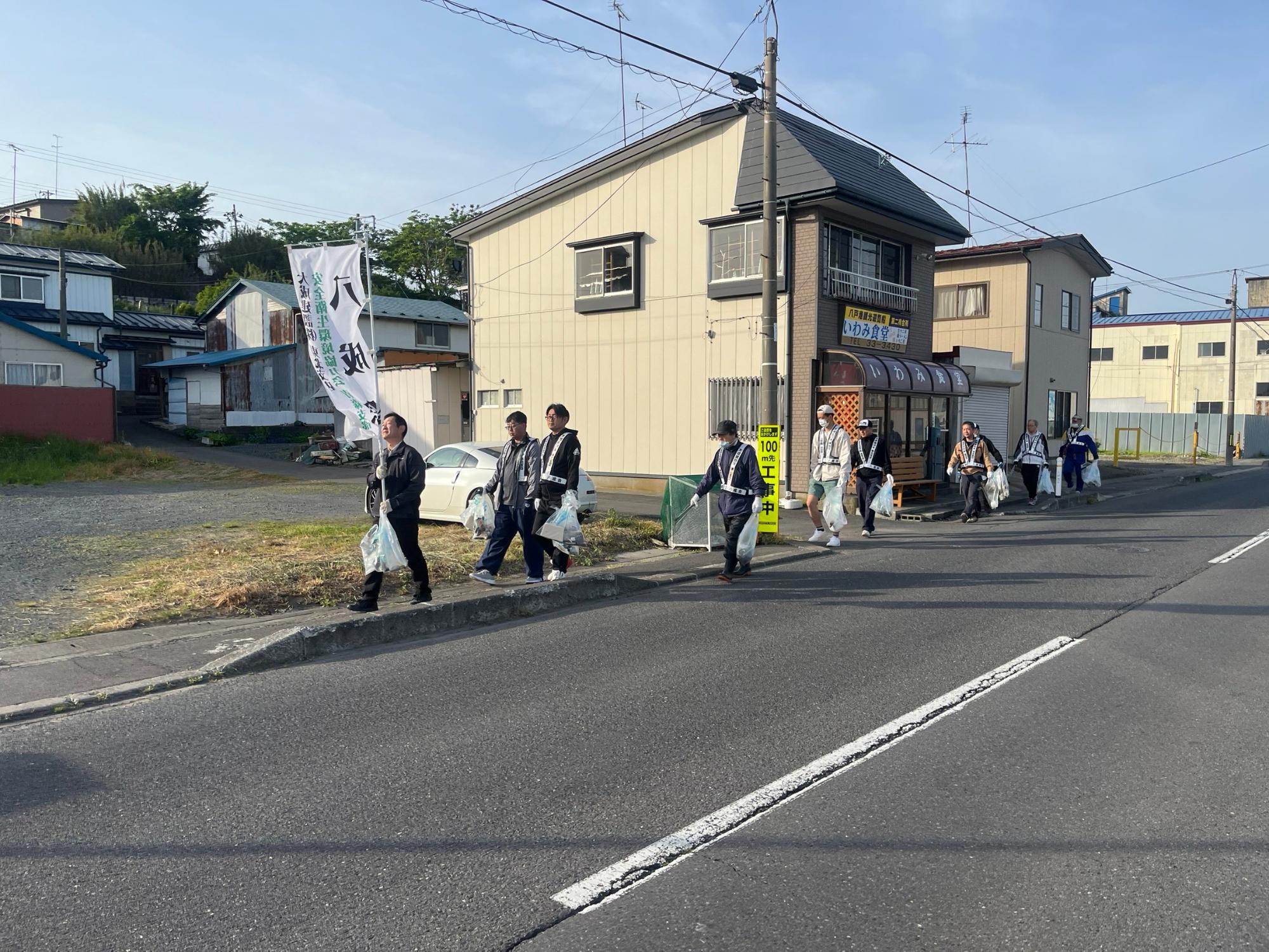 のぼり旗を掲げて歩道のごみを拾っているメンバーの写真
