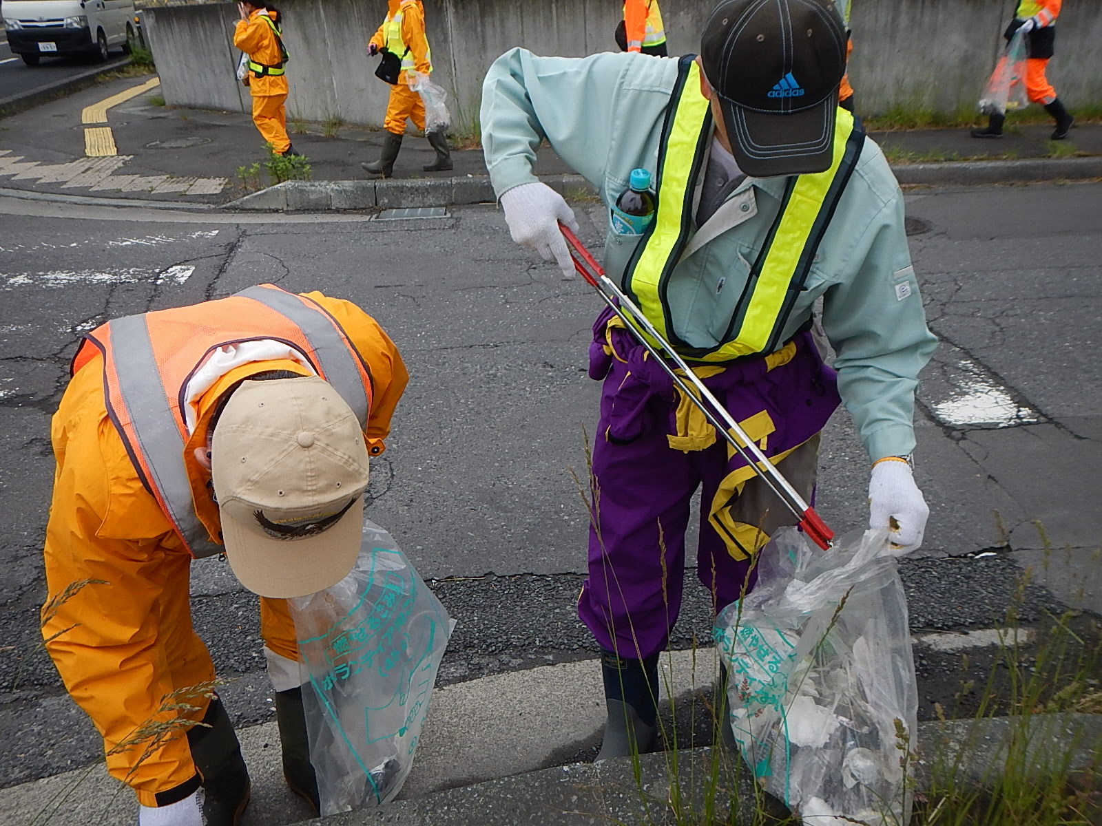 作業服姿で歩道のごみをトングで拾っている写真