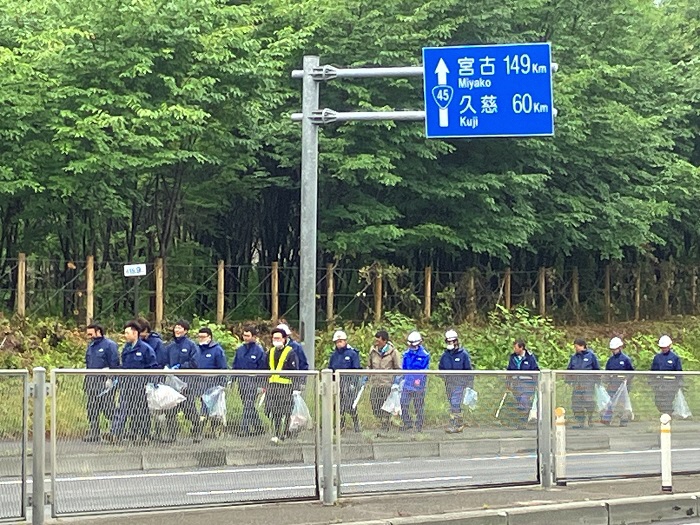 国道脇の歩道をごみ袋、トングを手に大人数で歩いている写真