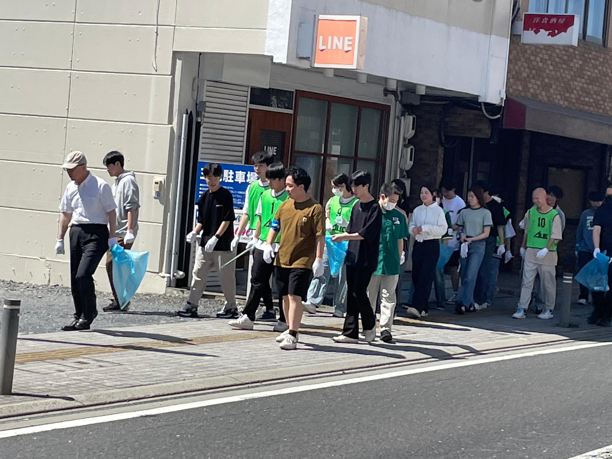 中心街の歩道のごみを拾うべくビブスを着用し、大勢で歩いている写真