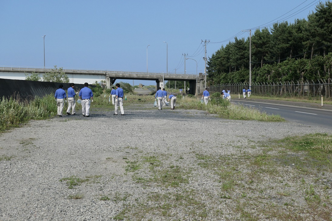 道路脇の広い場所のゴミを拾っている10数人の写真