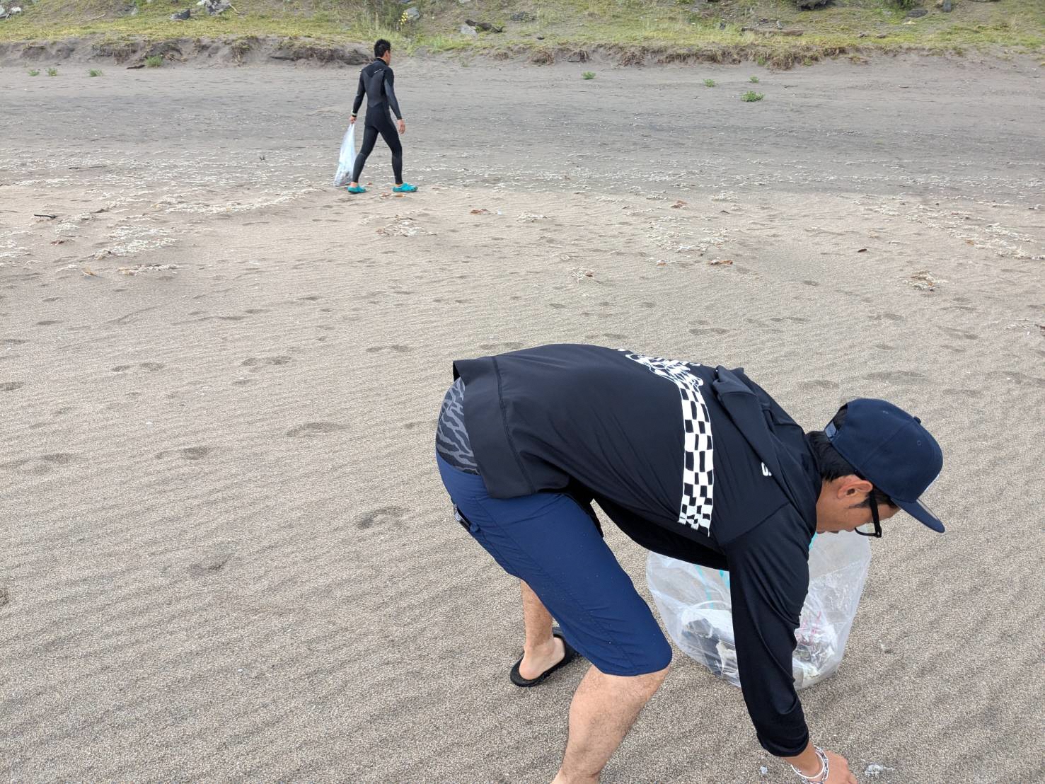 砂浜でボランティア用ごみ袋を持ってごみを拾っている男性の写真