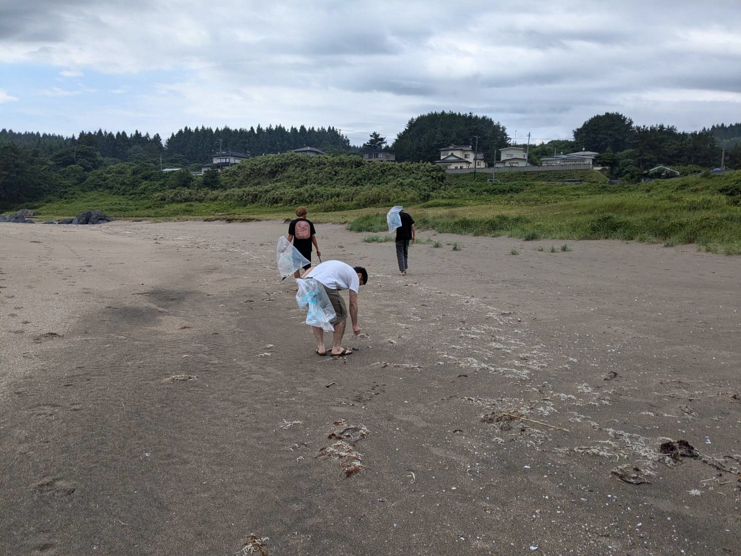 砂浜でボランティア用ごみ袋を持ってごみを拾っている写真