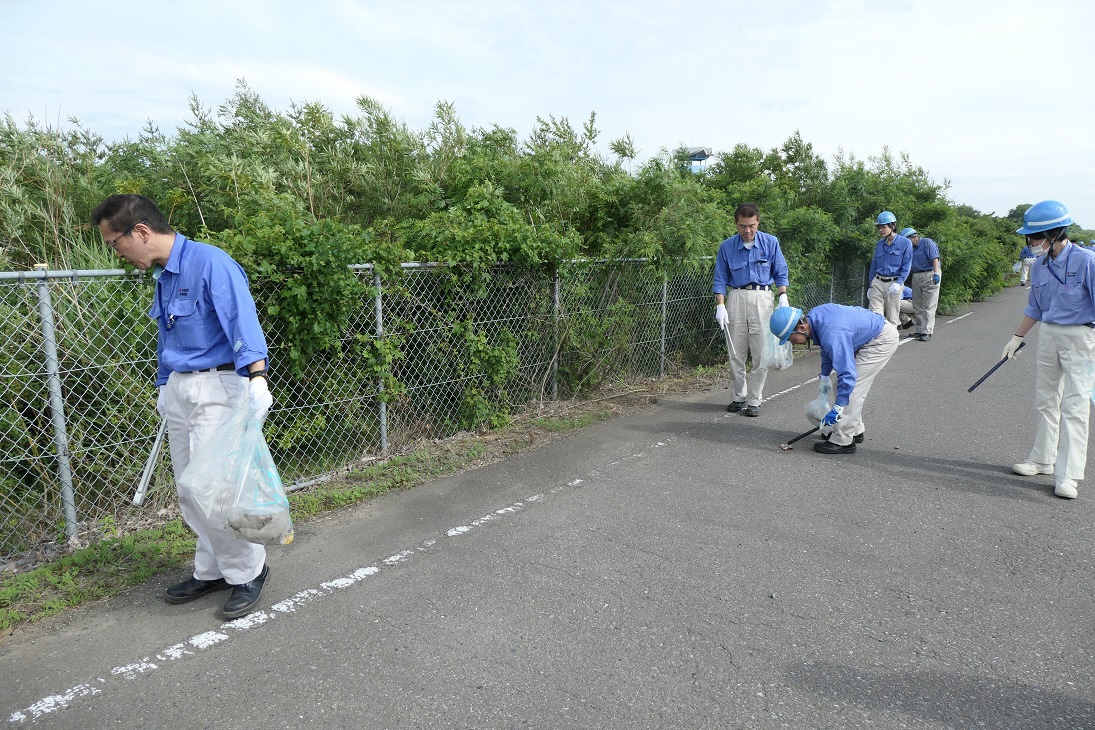 ヘルメットに作業服で歩道のごみを拾っている写真