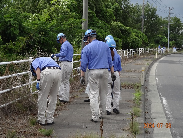 ヘルメットに作業服で歩道のごみを拾っている写真