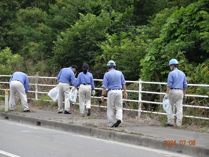 ヘルメットに作業服で歩道のごみを拾っている写真