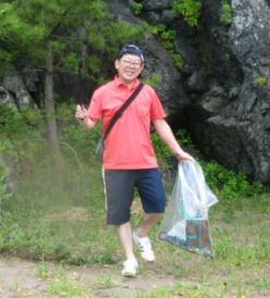 大きな岩の前で、燃やせないごみ袋を手にしているポロシャツ姿の男性の写真