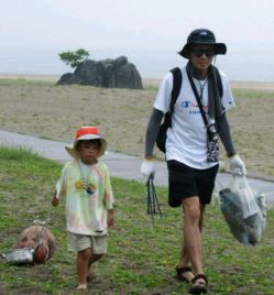 大きな岩の見える場所。トングとボランティア用ごみ袋を手に活動している子供と男性の写真。