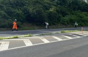 道路の向かい側からヘルメット作業服姿の三人を映した写真