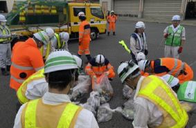ヘルメットに作業服、安全帯を着用した人たちが集めたごみを分けている写真