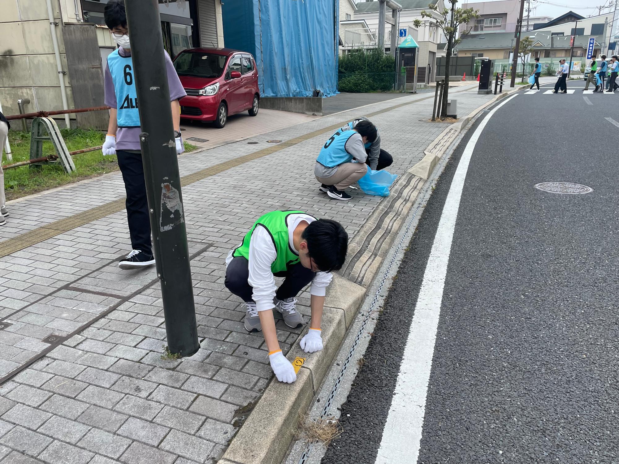 しゃがんで歩道に貼られたテープをはがしている男子学生の写真。