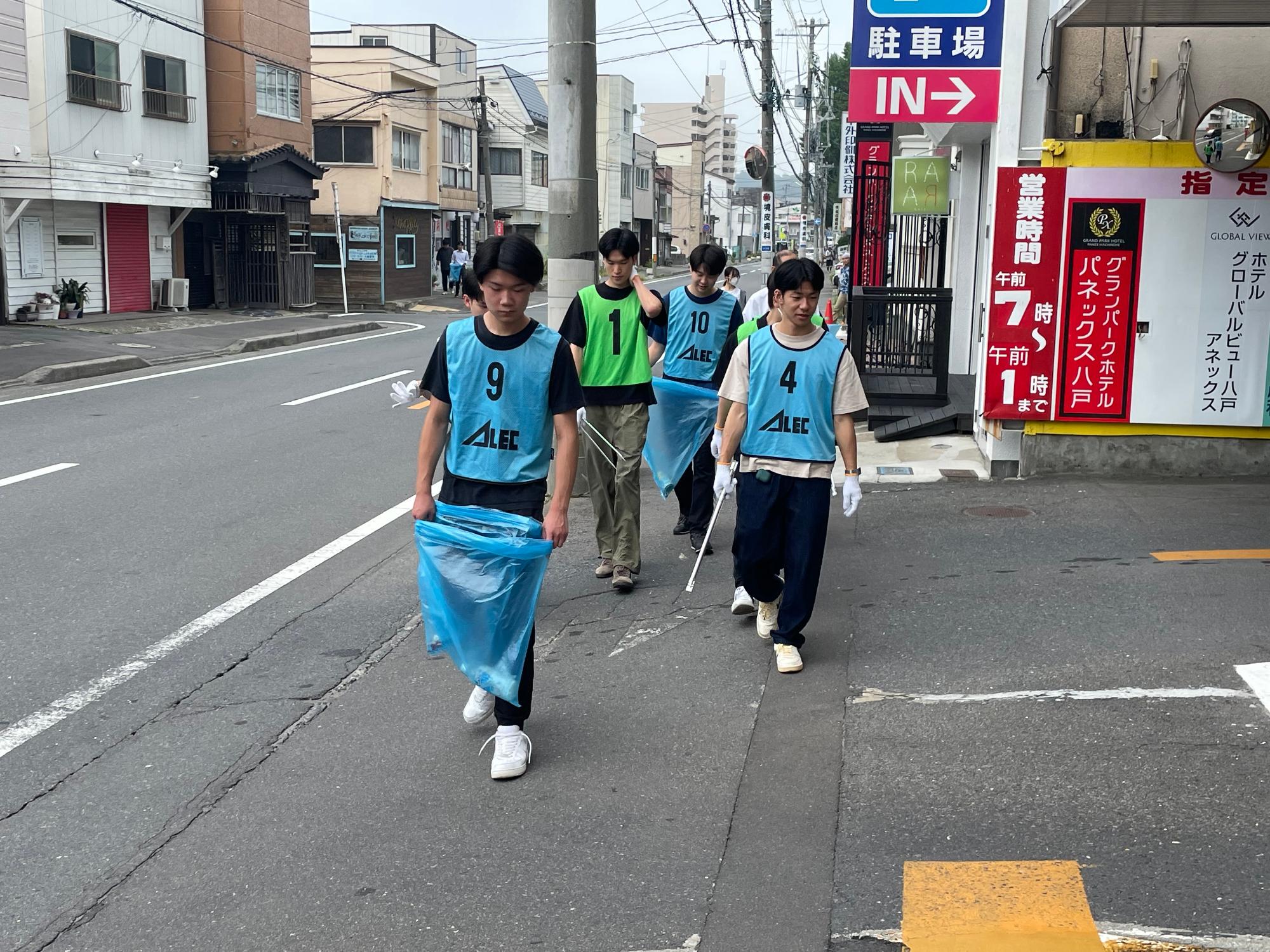 青色のビブスを着用し、歩道を歩く四人の男子学生の写真。
