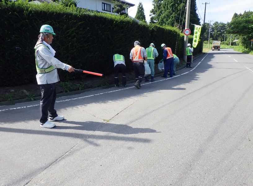 道路清掃中の幟を立てて、道路脇のごみを拾っている、ビブスを着用した人たちの写真