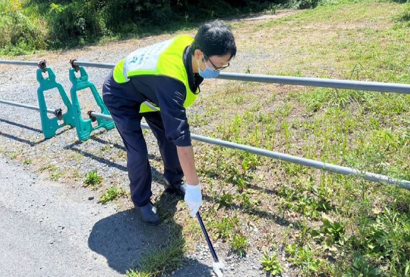 クリーンパートナーと書かれたビブスを着用し、草地のごみをトングで拾っている男性の写真