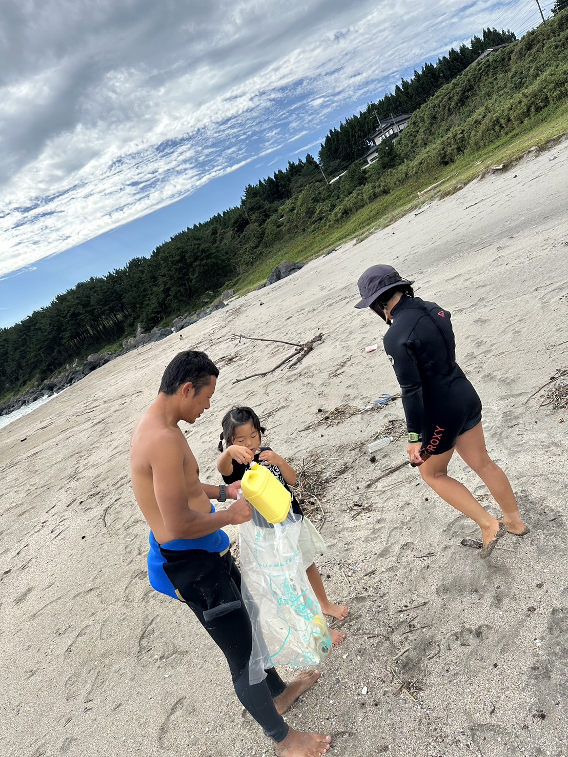 砂浜で拾ったごみをボランティア用ごみ袋に入れている子どもと大人二人の写真